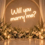 Beyaz çiçekler ve mumlarla süslenmiş kemerli bir duvarda günışığı renginde Will you marry me LED neon evlilik teklifi yazısı