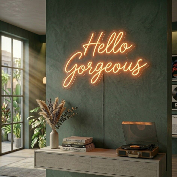 Yeşil tonlu duvarda ahşap konsolun üzerinde, sıcak sarı ışıkla iki satır Hello Gorgeous yazılı LED neon tabela