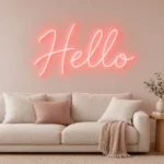 Açık pembe salon duvarında krem koltuk üzerinde Hello LED neon yazısı