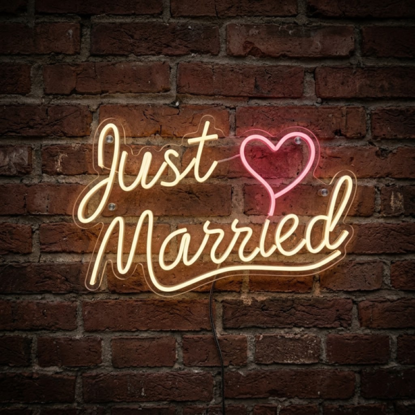 Koyu tuğla duvarda sıcak sarı Just Married yazısı, pembe kalp ve kavisli alt çizgiden oluşan LED neon tabela