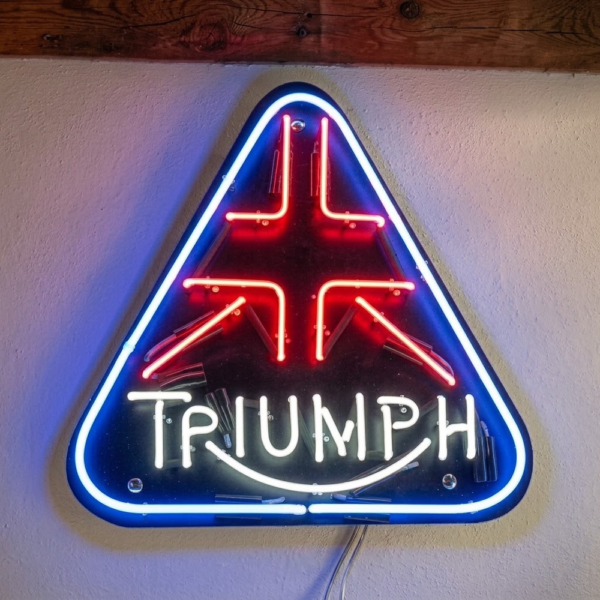 Mavi üçgen çerçeveli, kırmızı amblem çizgileri ve beyaz Triumph yazısı bulunan cam neon tabela