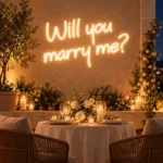 Mumlar ve beyaz güllerle süslenmiş iki kişilik teras masasının arkasında günışığı renginde Will you marry me LED neon yazısı